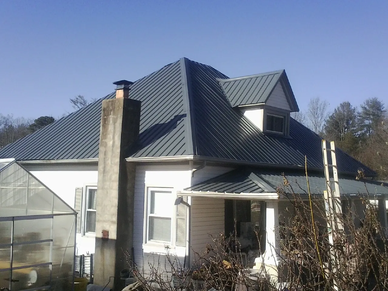 Dark blue standing seam metal roof on a white farmhouse with dormer — Slate & Tile Roof Repair by Roofing Brothers in Two Dot