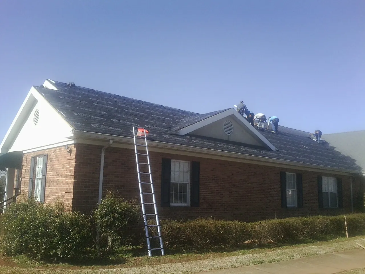 Crew tearing shingles off a brick ranch roof with a ladder set — Metal Roof Repair work by our crew in Two Dot