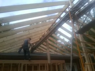 Rafters going up over a new addition with a worker on the wall in Two Dot