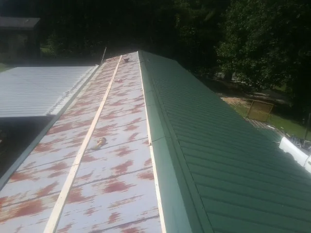 Old rusted panels beside newly installed green metal roofing — Wind Damage Roof Repair by Roofing Brothers in Two Dot
